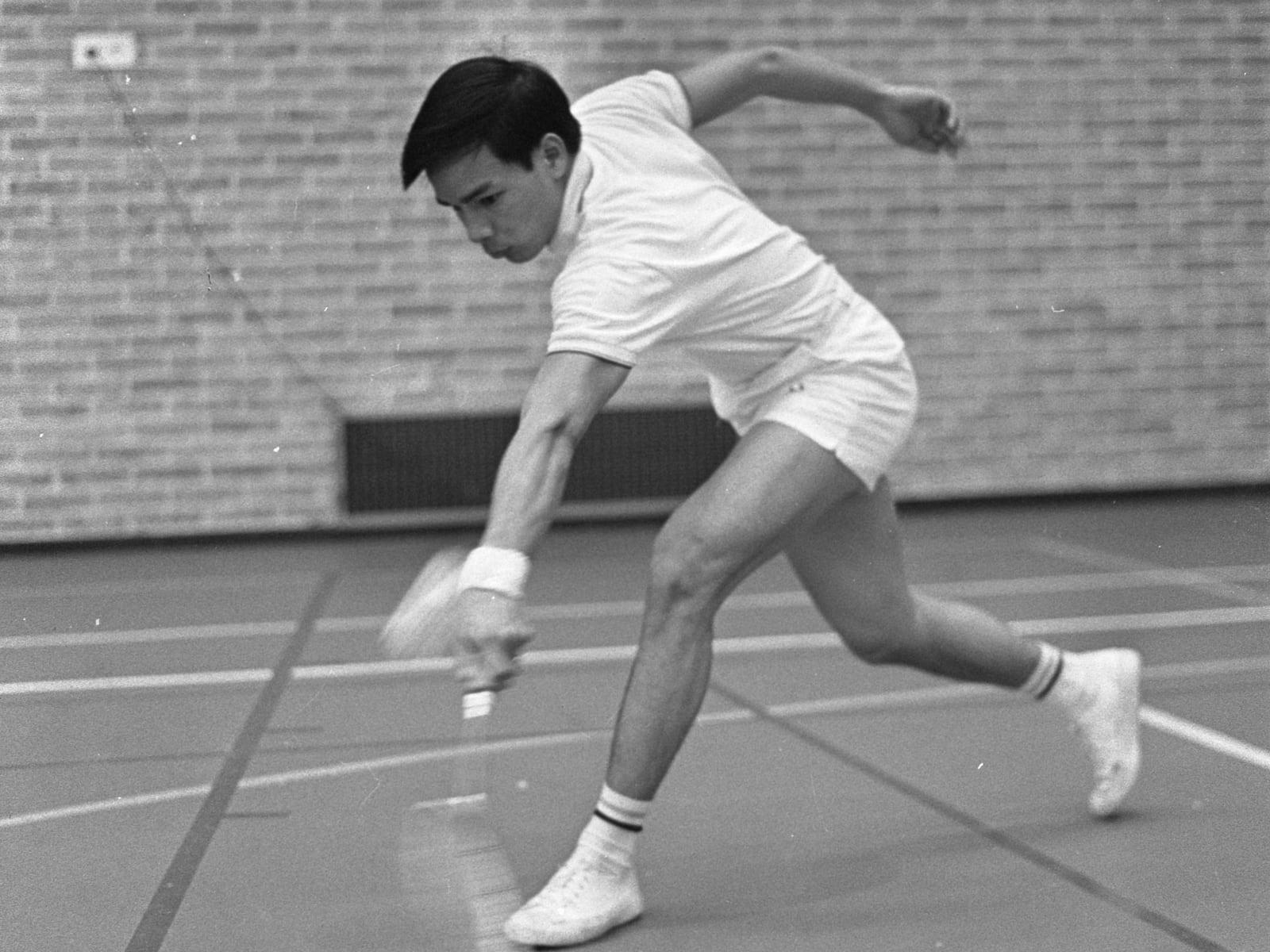 A badminton player driving at the shuttle on an indoor court, 1968